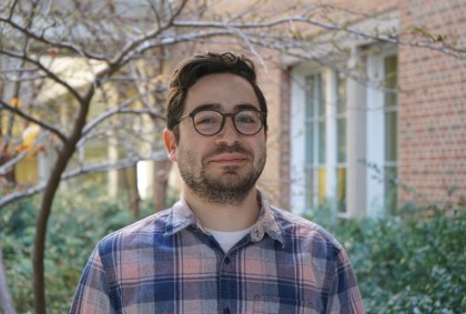 A man with brown hair and glasses in a blue and orange plaid shirt/