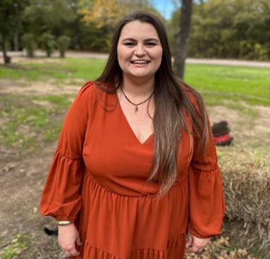 A person with long brown, straight hair in an rustic dark orange, long sleeve dress.