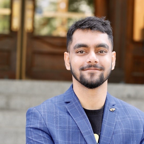 A person with somewhat wavy, short cut black hair in a checkered blue blazer