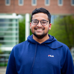 A grinning person with black close cut hair and a goatee in glasses and a blue FILA sweatshirt.